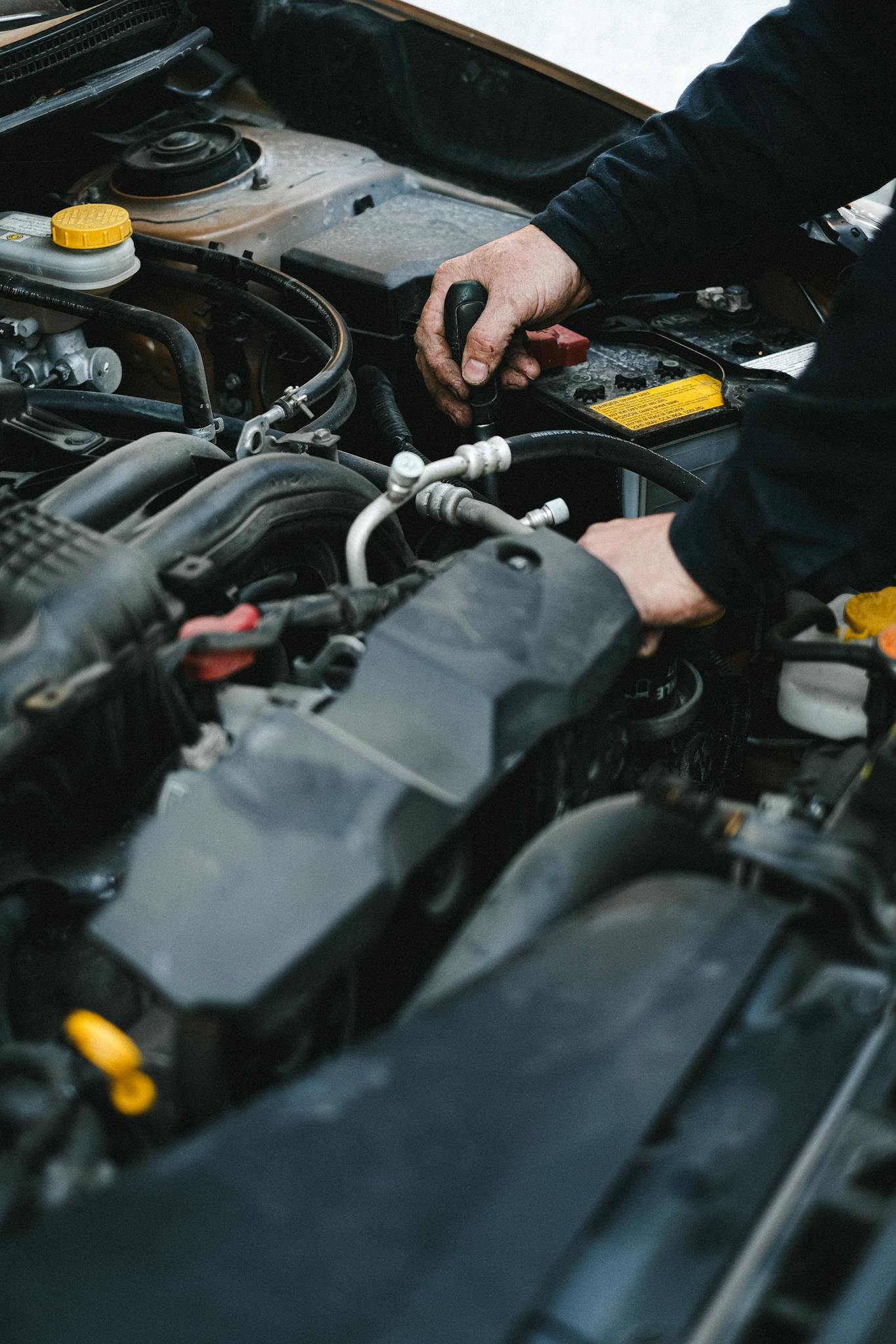 Close-up of a mechanic's hands working on a car engine in an indoor workshop setting.